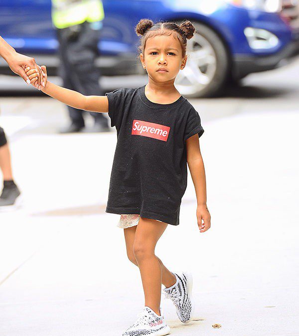 A little girl wearing a supreme t - shirt walking down the street.