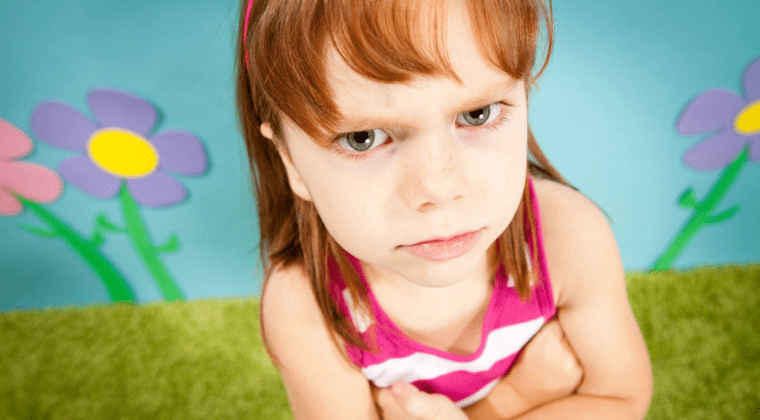 A little girl is sitting on the grass with flowers in the background, talking to kids about anger.