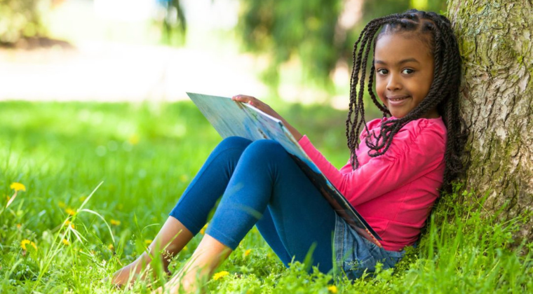 A little girl is sitting under a tree reading a book, helping kids calm down under stress