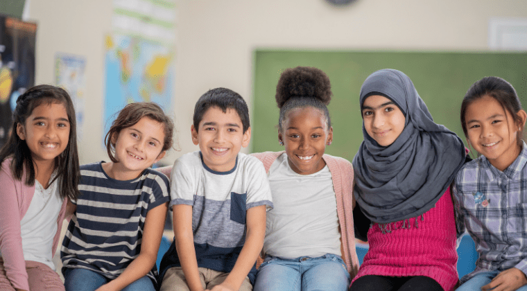 A group of children sitting together in a classroom, displaying inclusivity and acceptance towards people who look different.