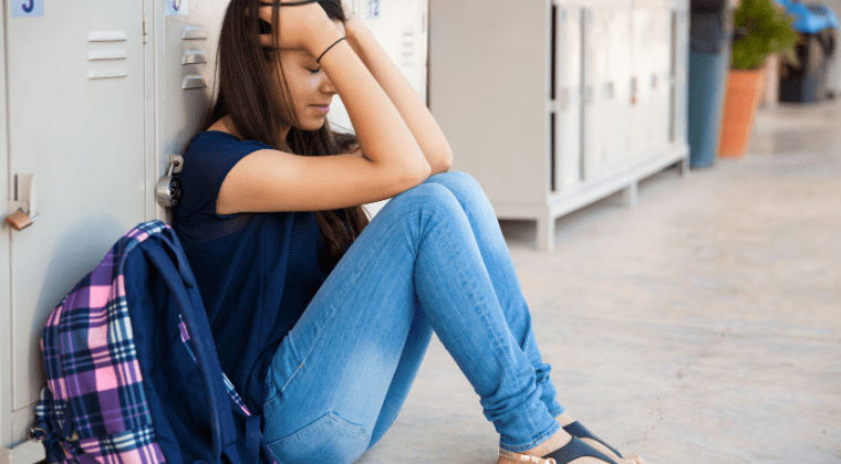 A girl sitting near a locker with hands on the head